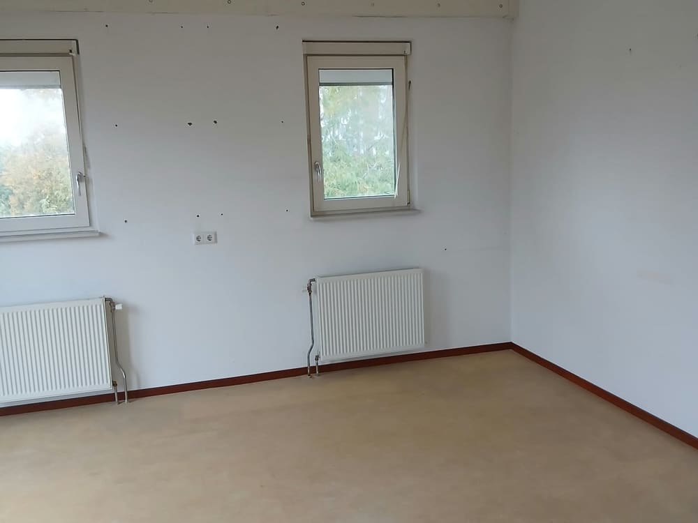 Leeg vertrek met ramen en radiatoren, bezemschoon achtergelaten